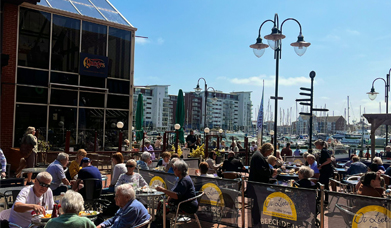 Tables of people eating outside in the sunshine with Sovereign Harbour in the background